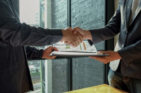Businessman shakehand and exchanging contract documents.